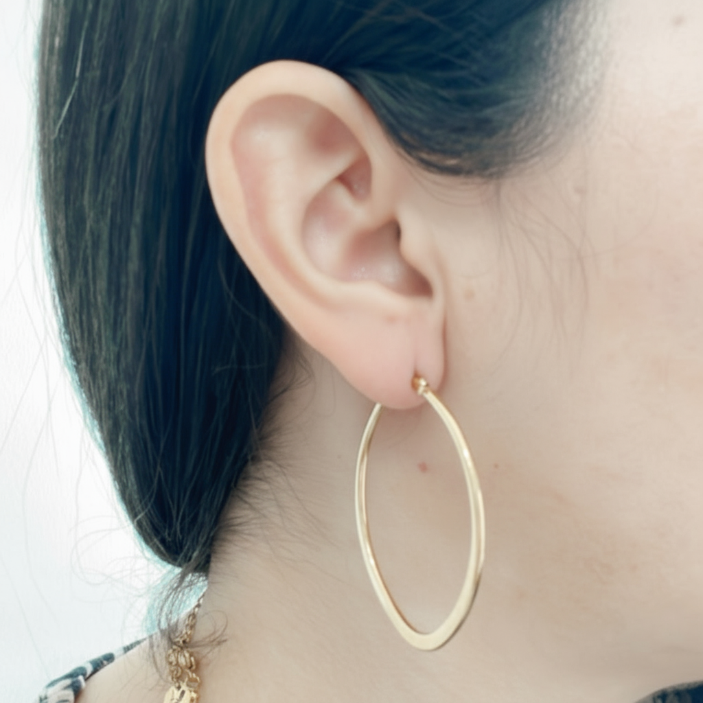 Modelo luciendo aros hoop dorados con forma de óvalo en acero inoxidable, estilo moderno de Vanytel Jewelry.