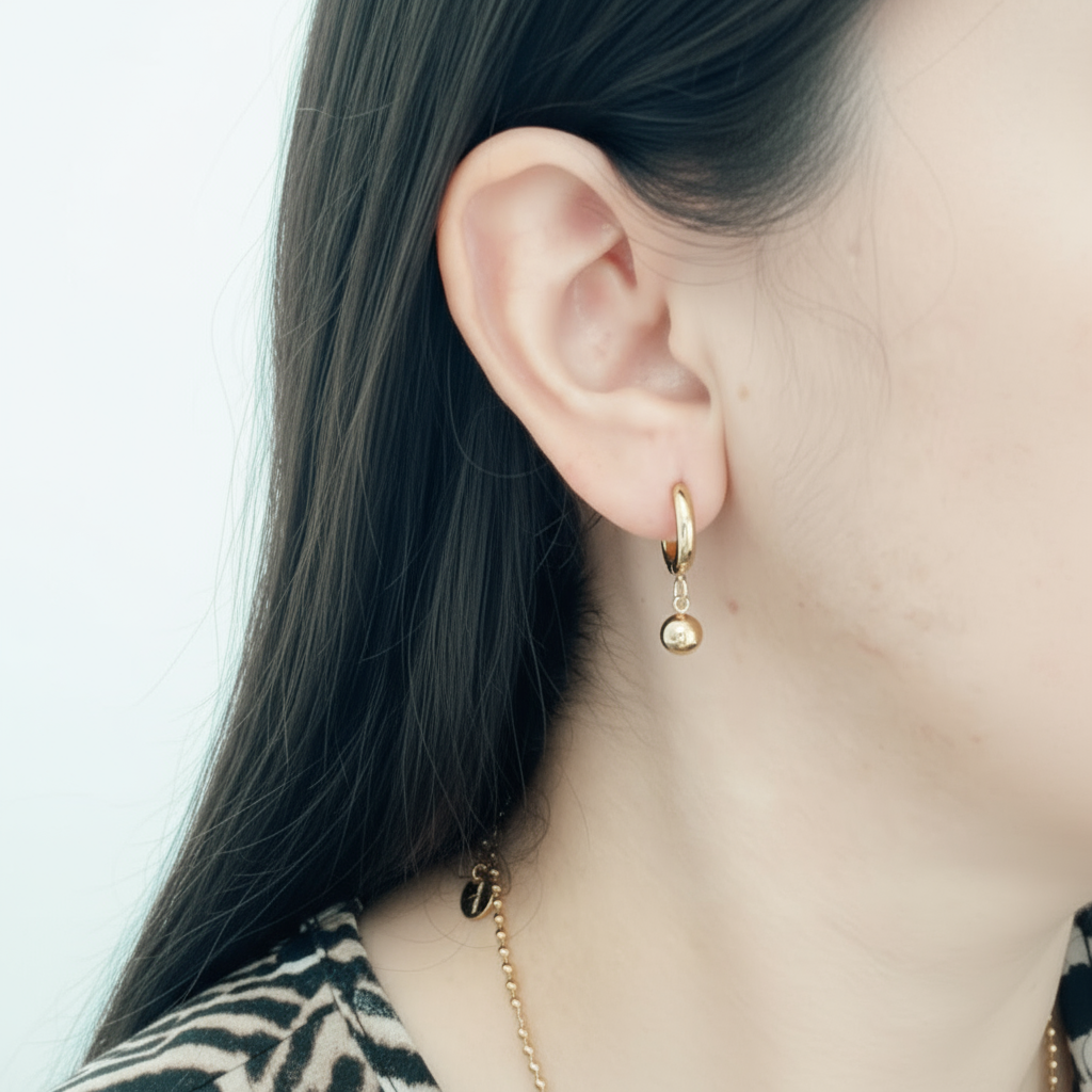 Mujer luciendo aros huggies dorados con bolita de acero inoxidable Vanytel, estilo moderno y cómodo para uso diario.