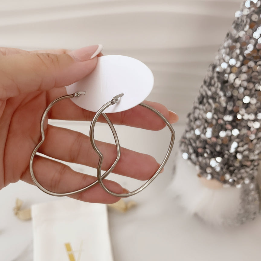 Aros hoop de corazones plateadas sobre mano de exhibición, joyería Vanytel.