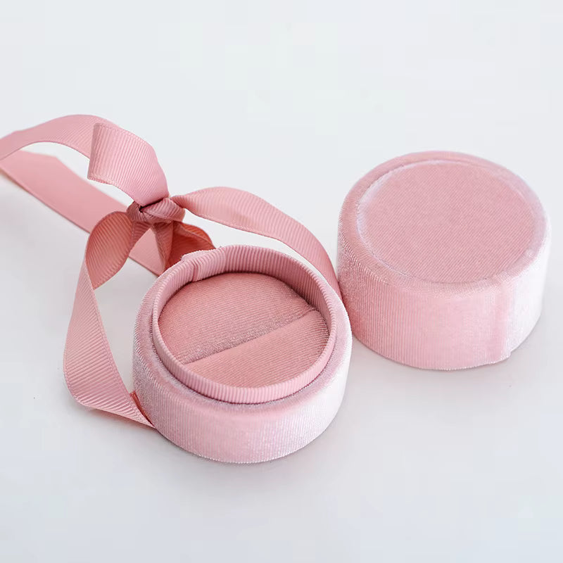Caja de terciopelo rosa Vanytel para anillo, abierta mostrando su interior acolchado y cinta decorativa.