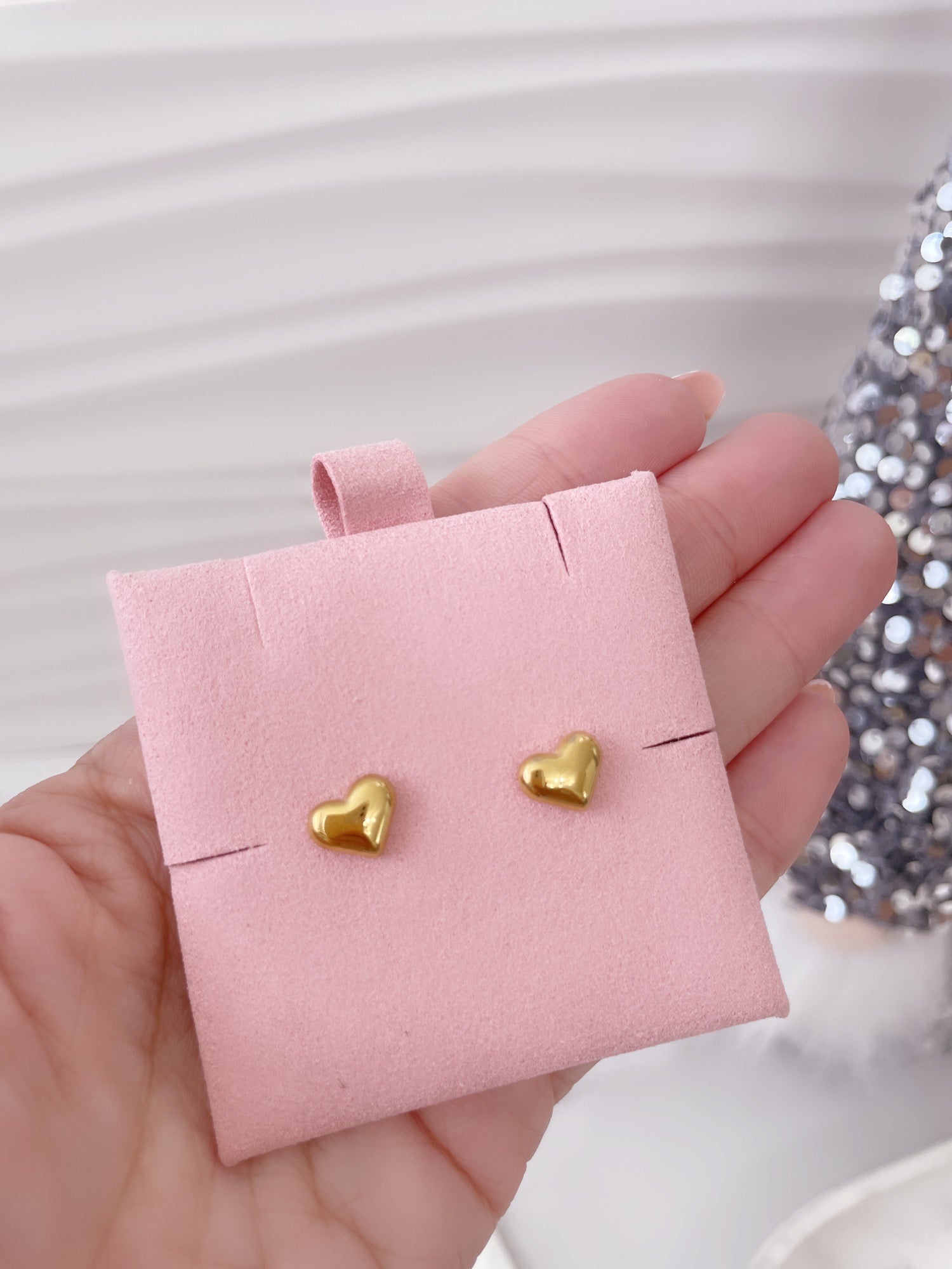 Conjunto de aretes dorados tipo stud sostenidos con la mano, Vanytel.
